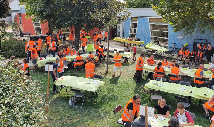 Dejeuner dans un jardin. Une soixantaine de participants, portant un gilet orange, autout de tables.